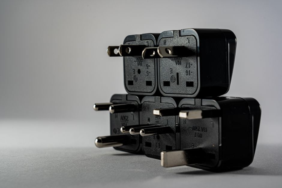 A close-up of a black universal travel adapter with multiple plug configurations and USB ports, sitting on a wooden table, ready for international use.