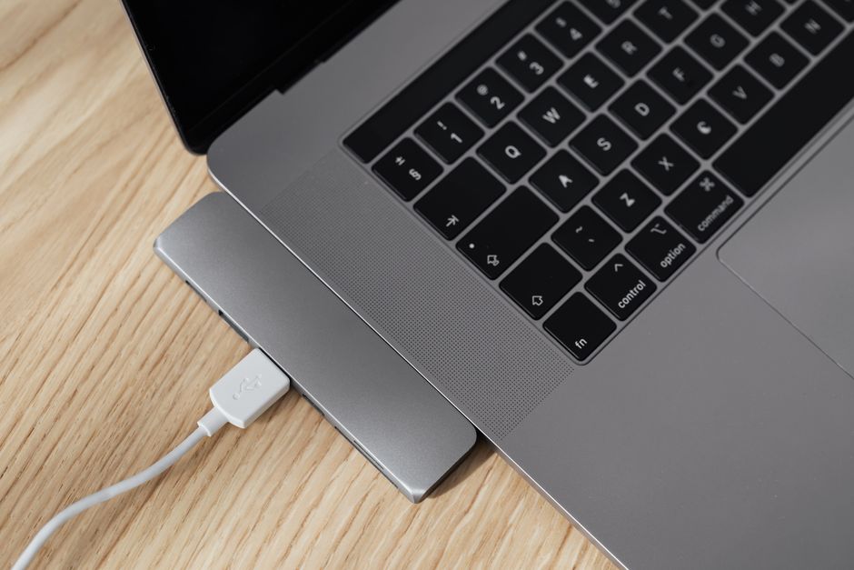 A sleek silver laptop connected to an external monitor and a keyboard/mouse via a single USB-C hub, showing a simplified desk setup.