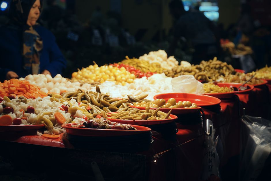 A vibrant display of various fermented foods on a wooden table, including jars of colorful kimchi, sauerkraut, a bowl of yogurt, and a bottle of kombucha.
