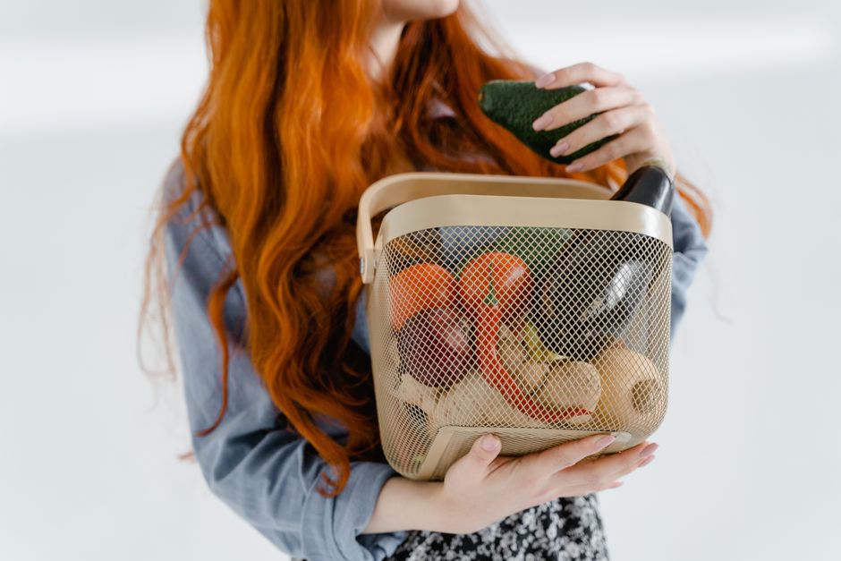 A person holding a large woven market basket filled with a variety of fresh produce, walking through a market.
