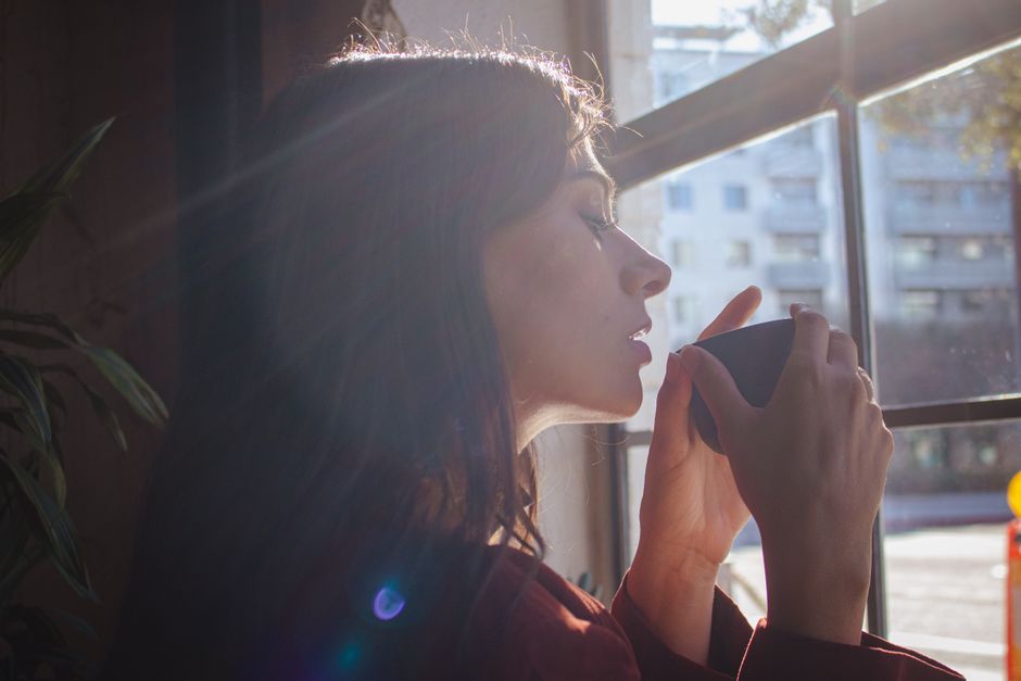 A person enjoying a cup of coffee by a bright window on a cloudy morning, demonstrating the importance of morning light exposure even in urban settings.