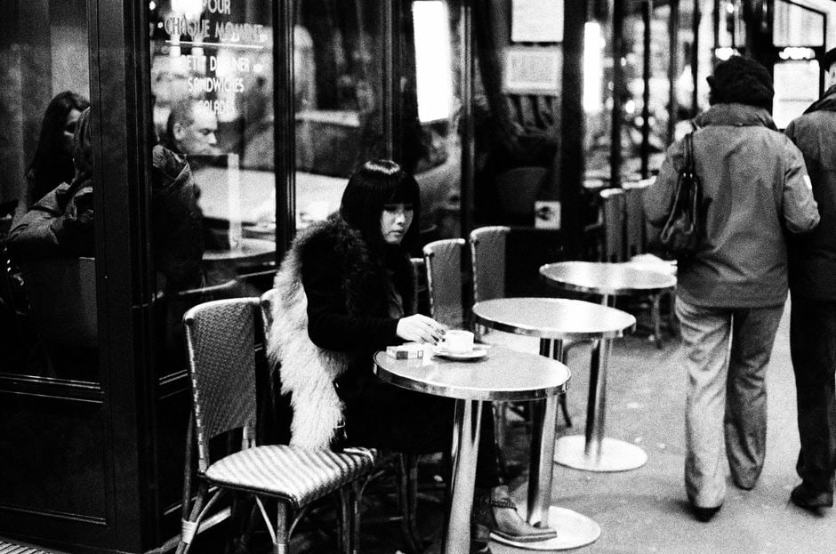 A woman smiling while sipping coffee at an outdoor cafe in Paris, enjoying a relaxed moment after a morning of exploration.