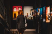 A woman admiring art in a gallery, dressed in smart casual attire: tailored trousers, a knitted sweater, and chic loafers.