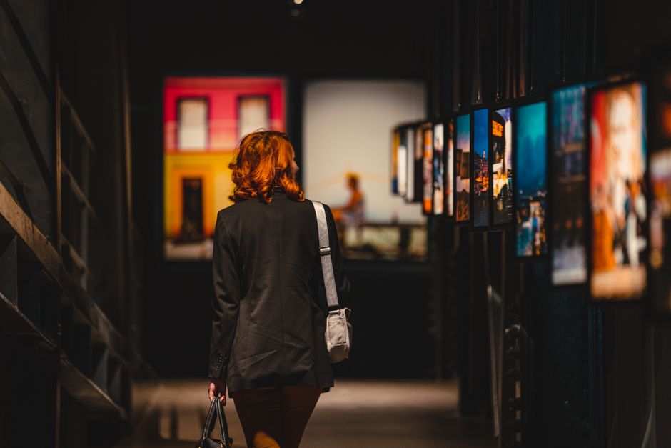 A woman admiring art in a gallery, dressed in smart casual attire: tailored trousers, a knitted sweater, and chic loafers.
