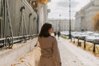 A stylish woman in a classic beige trench coat walks confidently down a European city street, embodying French elegance.