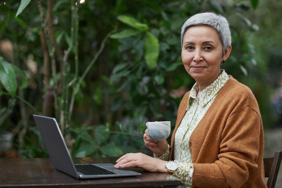 A woman wearing a chic tweed statement jacket, seated at an outdoor cafe with a laptop and coffee, looking sophisticated and relaxed.