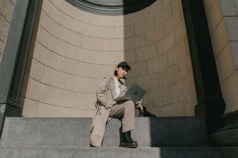 A woman confidently walking through a European city street, wearing a classic beige trench coat over a casual outfit, highlighting its versatility for various weather and occasions.