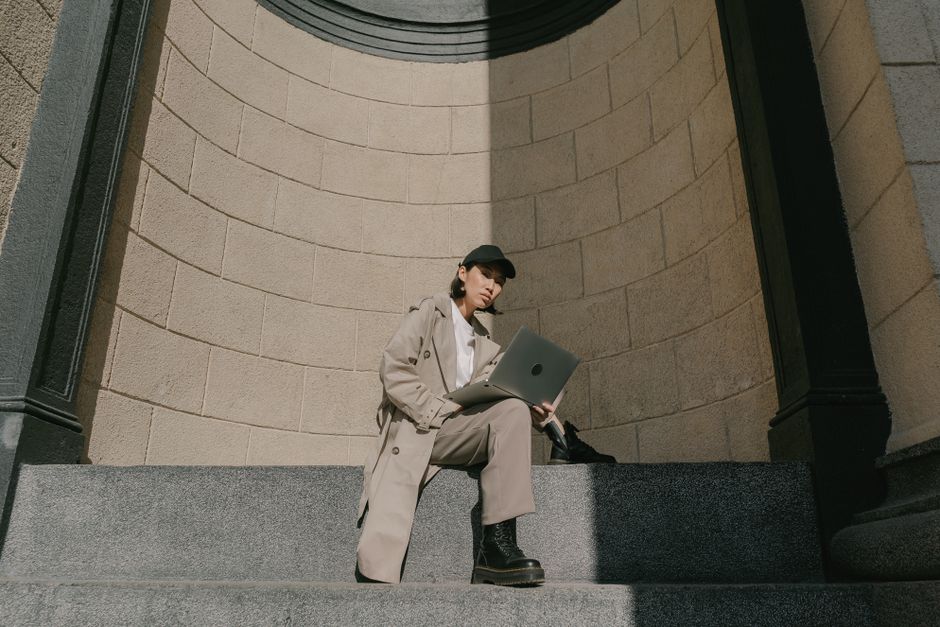 A woman confidently walking through a European city street, wearing a classic beige trench coat over a casual outfit, highlighting its versatility for various weather and occasions.