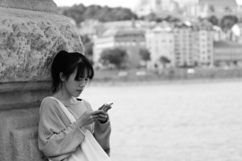 Woman looking at her phone for directions on a cobblestone street in a historic European city.