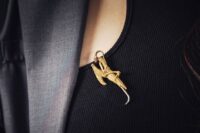 Woman's hand carefully pinning an ornate vintage brooch to the lapel of a gray wool blazer, showing how brooches add detail.