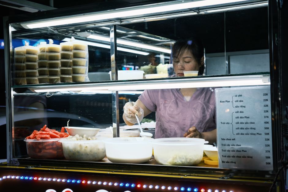 A woman in a modern kitchen, pre-portioning almonds and chopped vegetables into small containers for quick access during late work hours.