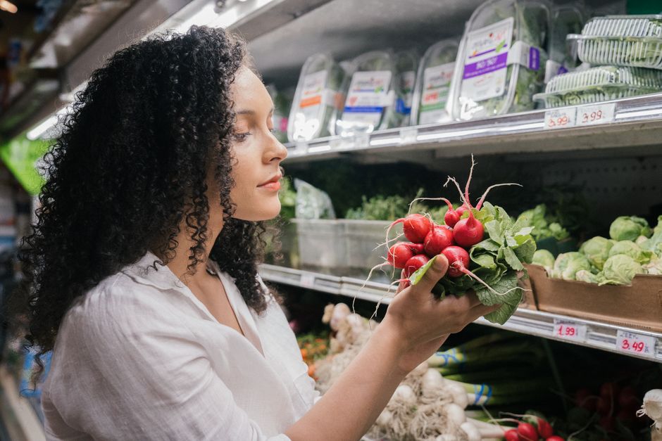 A woman's hands gently picking ripe, colorful bell peppers from a stall at an outdoor farmers market, with other fresh produce in the background.