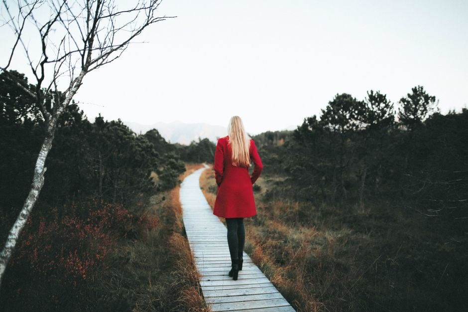 A woman walks thoughtfully on a path through a dense, colorful autumn forest, suggesting peaceful contemplation and a deliberate connection with nature.