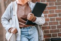 A stylish woman in a trench coat walks briskly on a city street, carrying a polished leather laptop bag, embodying city commuter style.