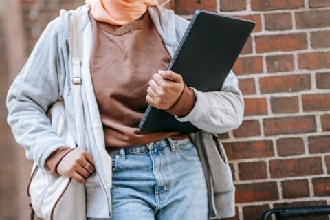 A stylish woman in a trench coat walks briskly on a city street, carrying a polished leather laptop bag, embodying city commuter style.
