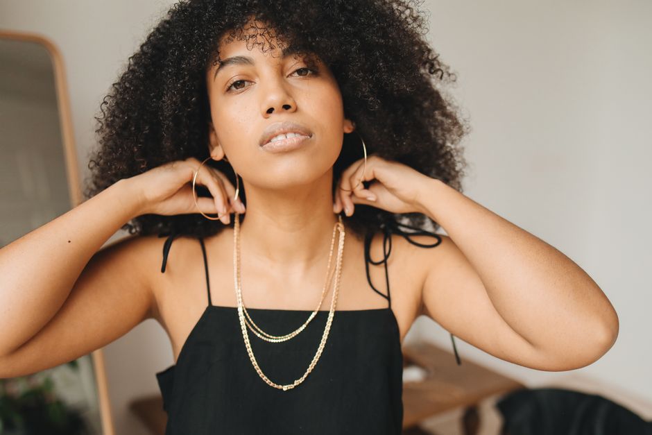 A close-up of a woman's ear adorned with a simple, elegant gold hoop earring, complementing a neutral-toned outfit, illustrating everyday minimalist style.